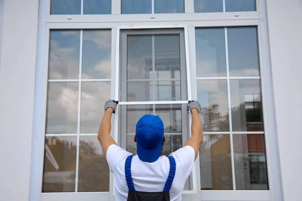 Worker in blue cap and white shirt installing or adjusting a window frame on a white exterior wall